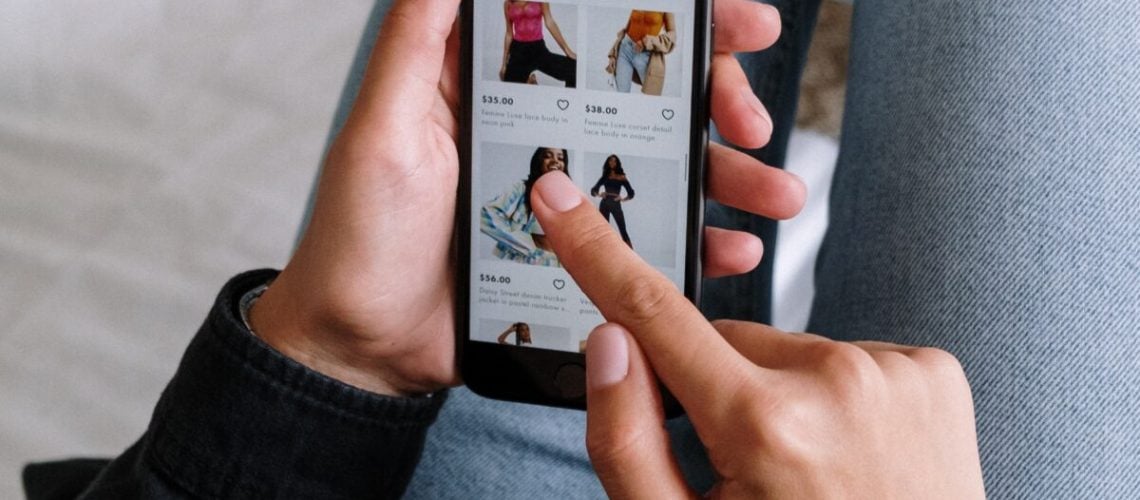 A man sitting on the sofa scrolling through products on an ecommerce website on his phone